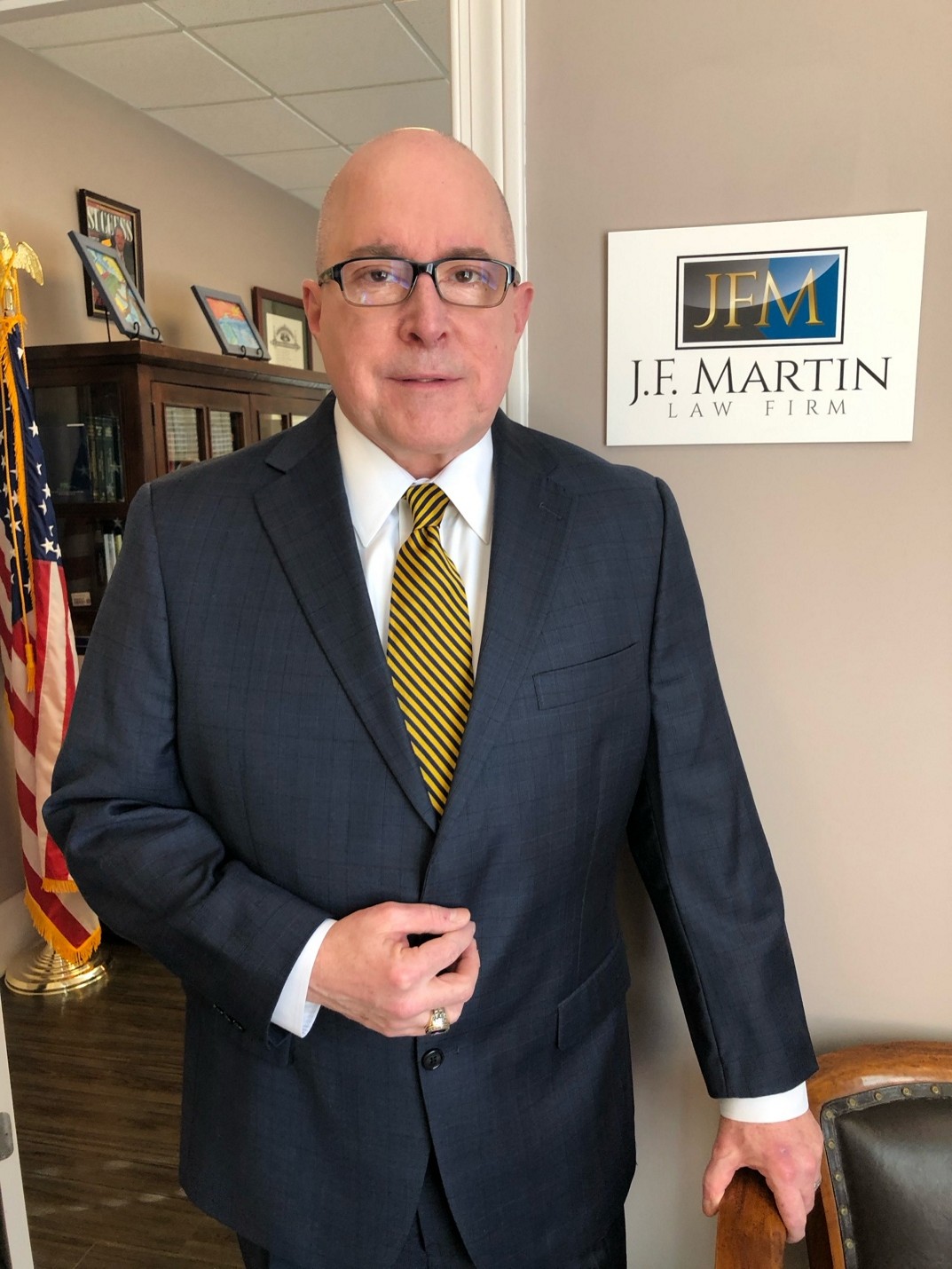 Man in suit and yellow tie standing indoors with a Je Martin sign.