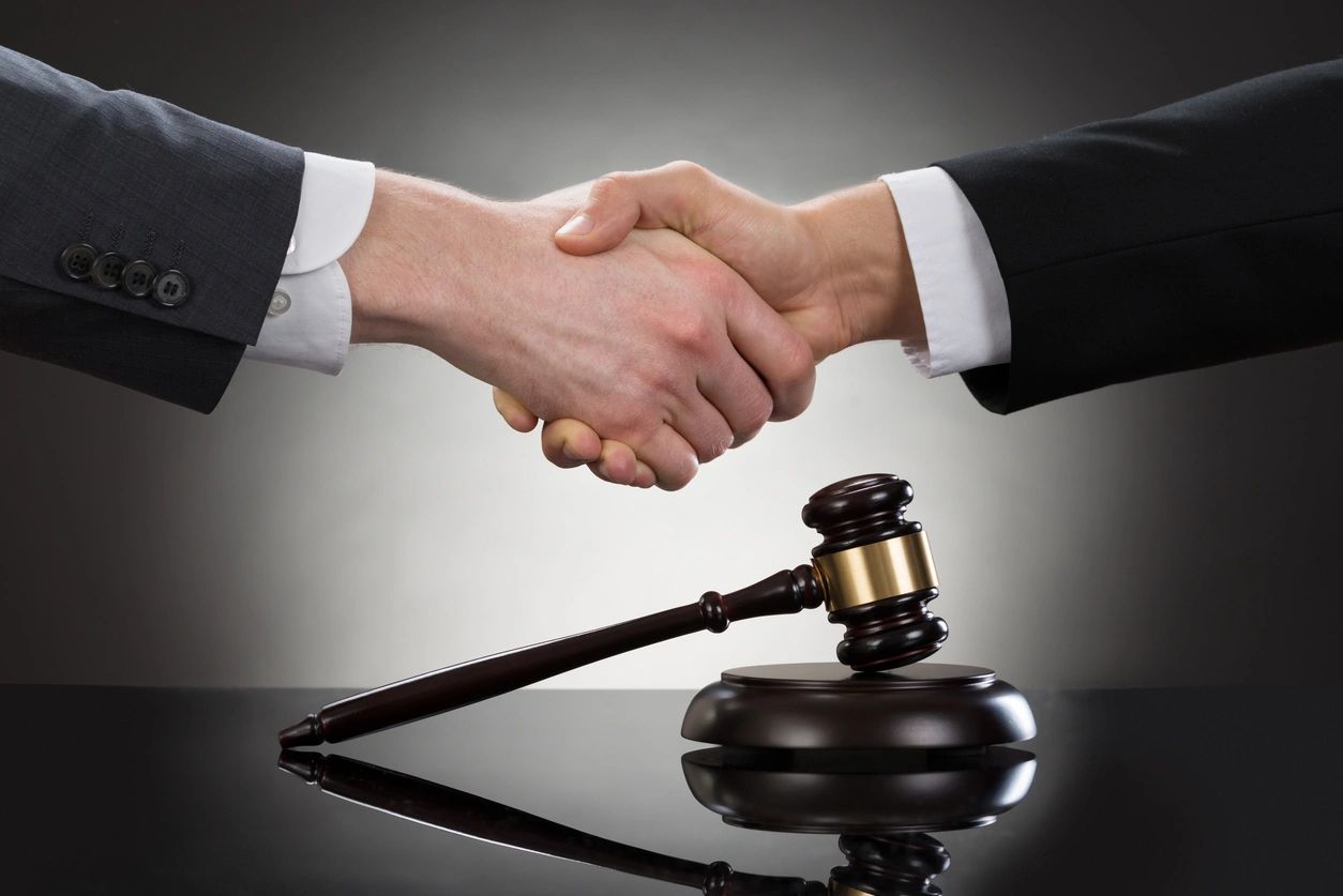 Two people in suits shaking hands over a judge's gavel.