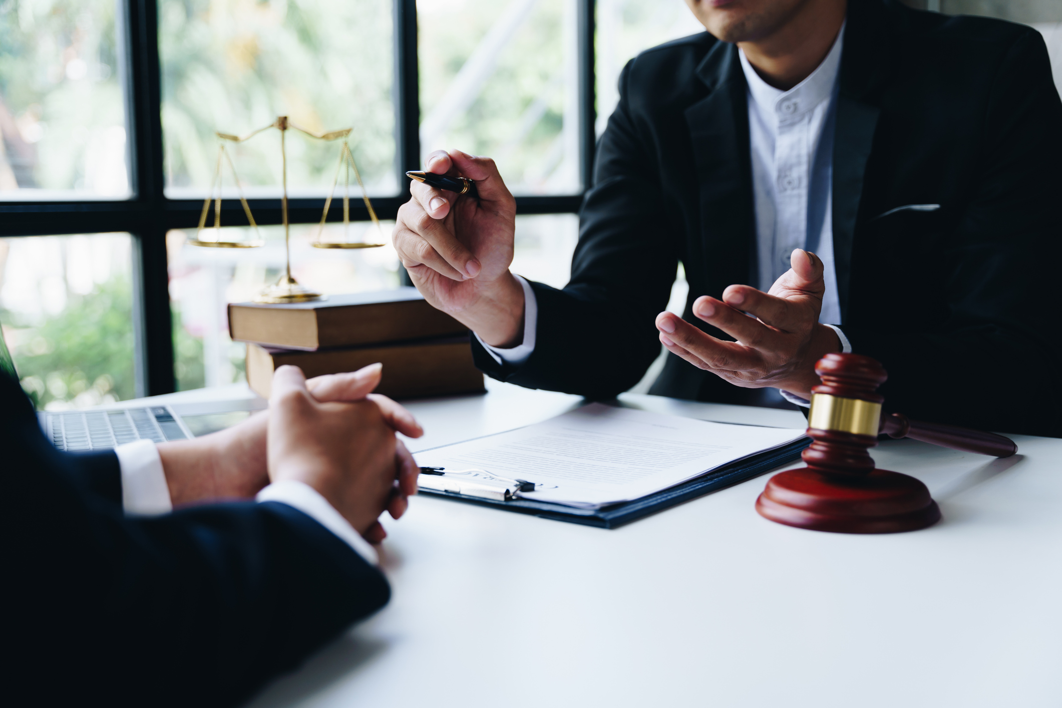 Lawyer consulting client with legal documents and gavel on table.