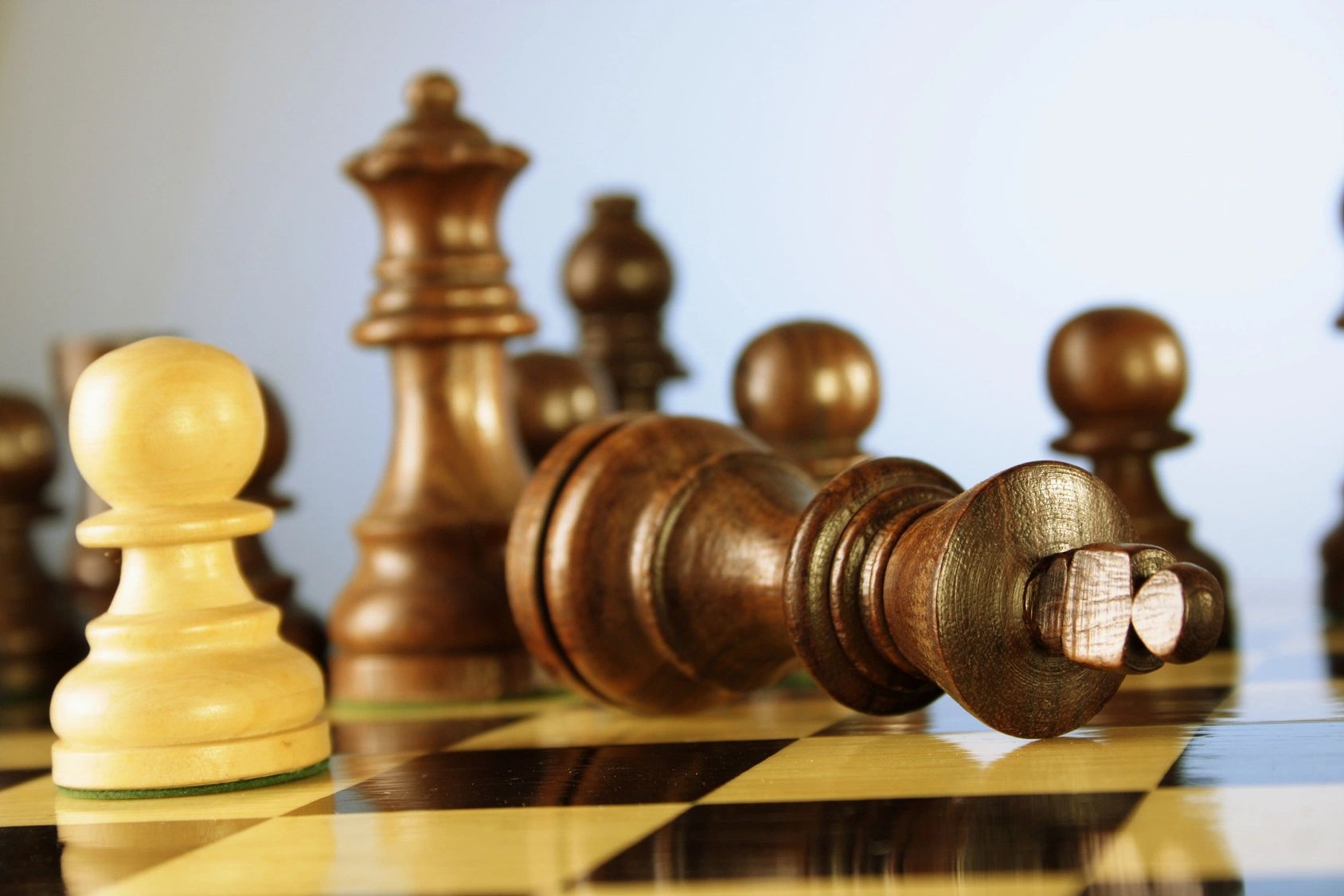 Wooden chess pieces on a board with a fallen king in focus.