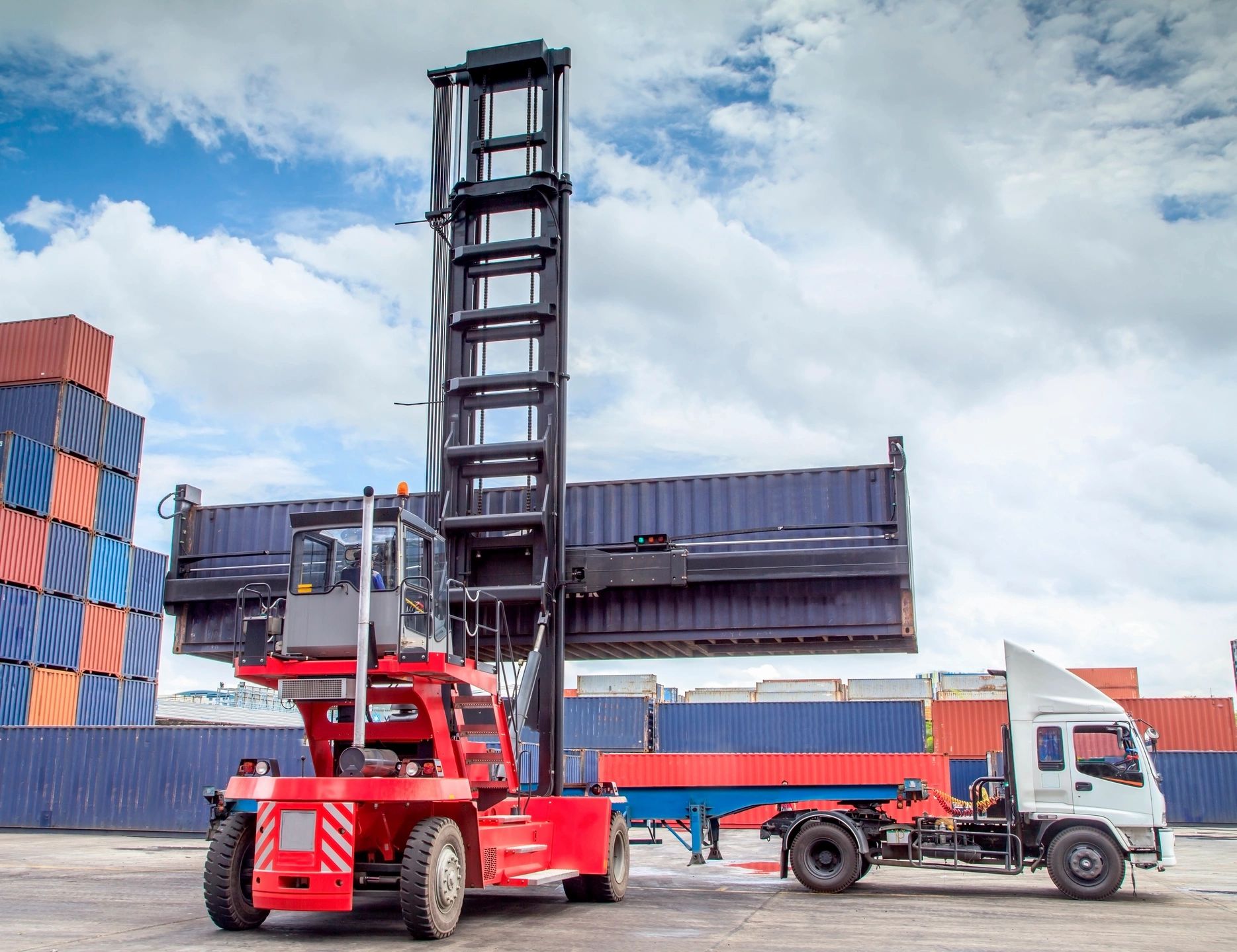 A large red container handler lifting a shipping container outdoors.