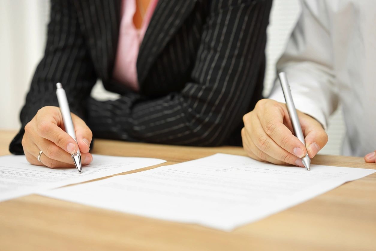 Two people signing documents at a table.