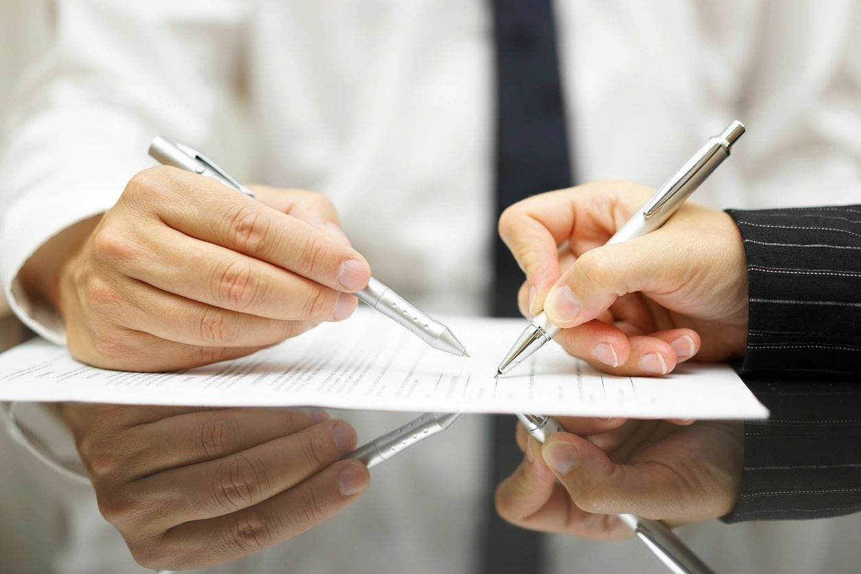 Two people signing a document with pens.