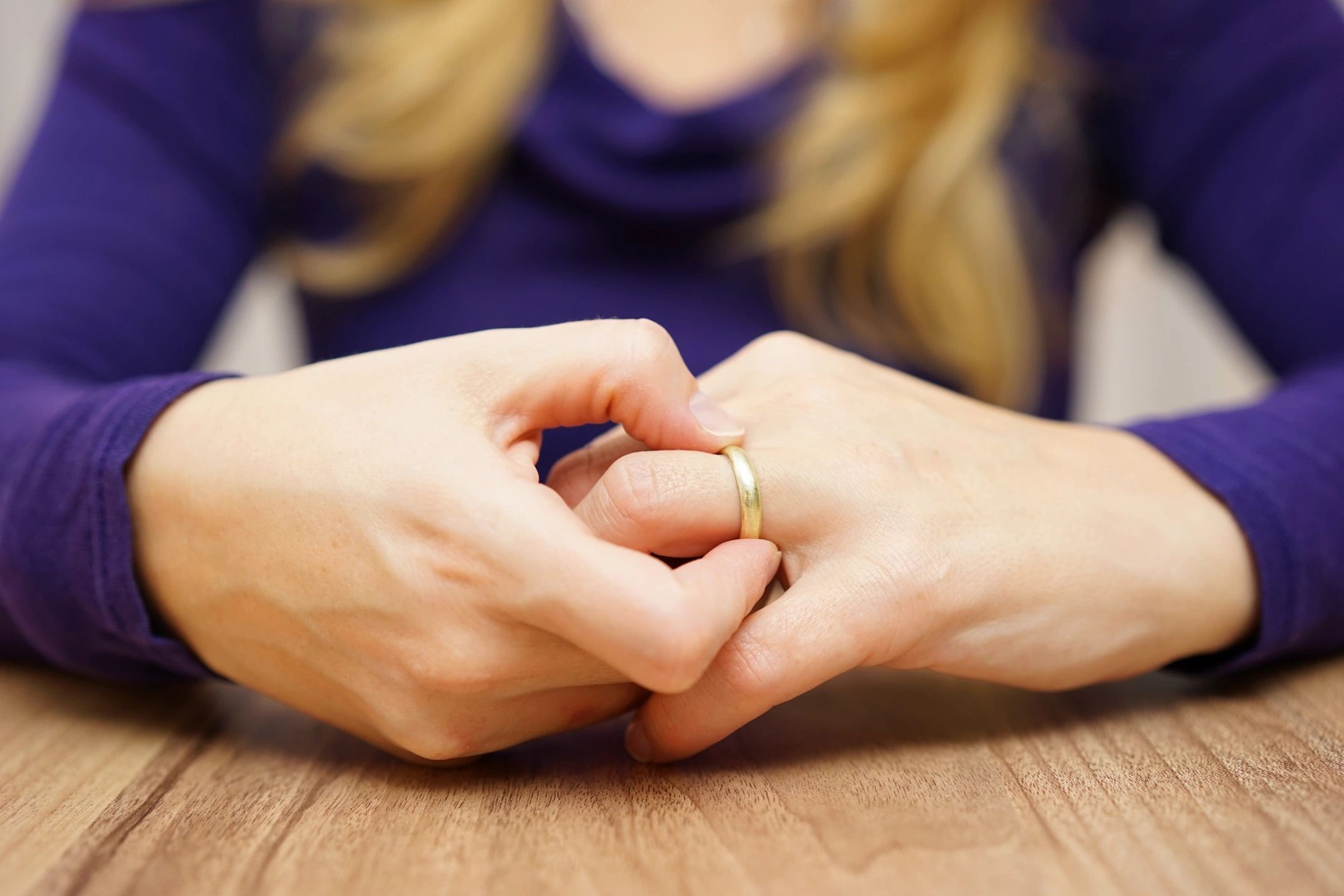 Close-up of hands with a wedding ring, fingers intertwined.