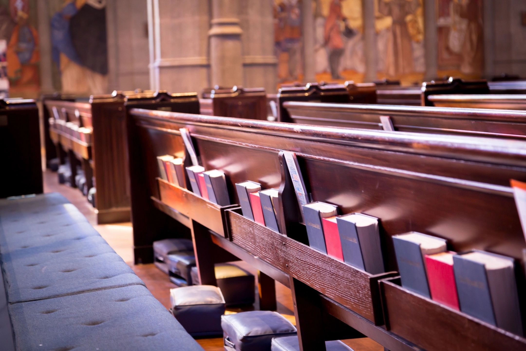 Rows of wooden church pews with hymnals and Bibles.