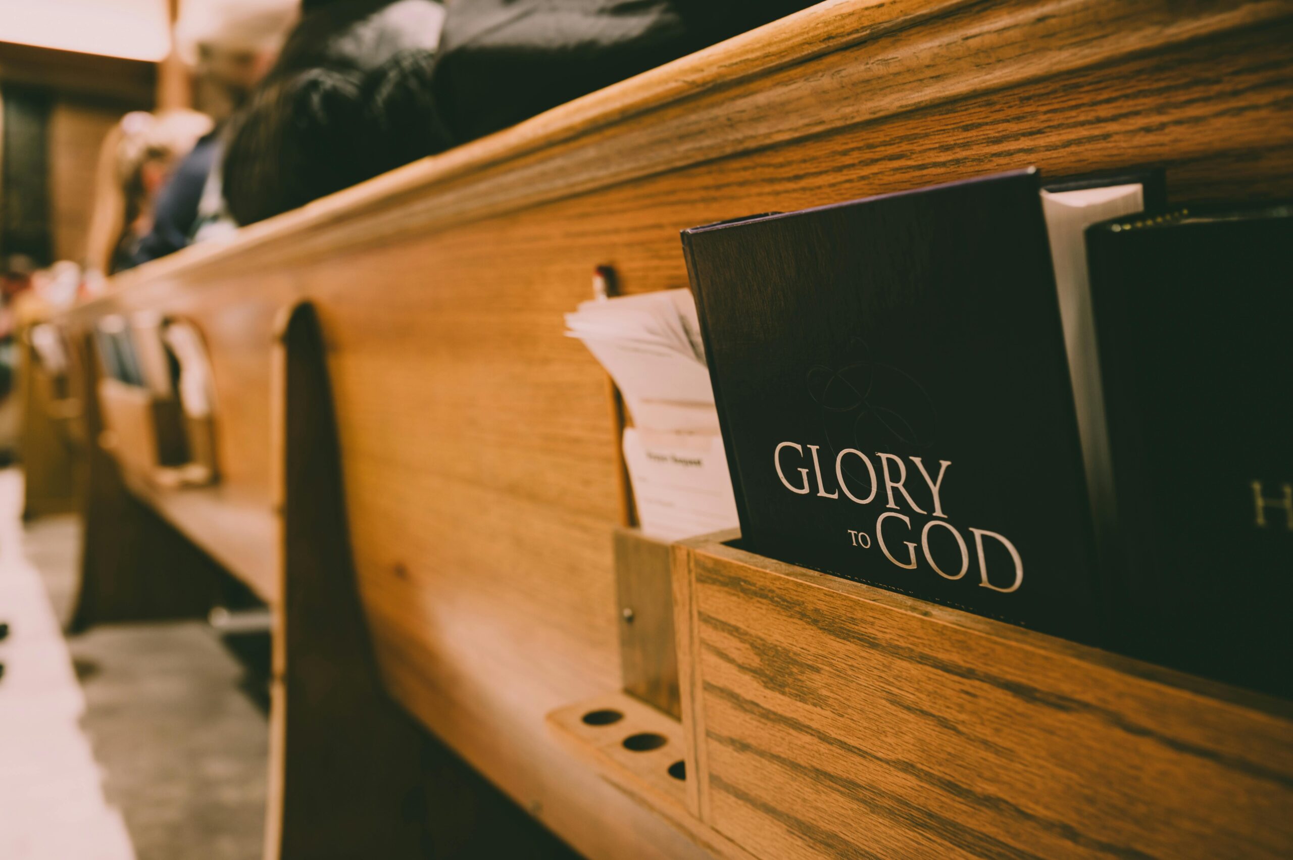 A Bible titled 'Glory to God' rests in a wooden church pew.