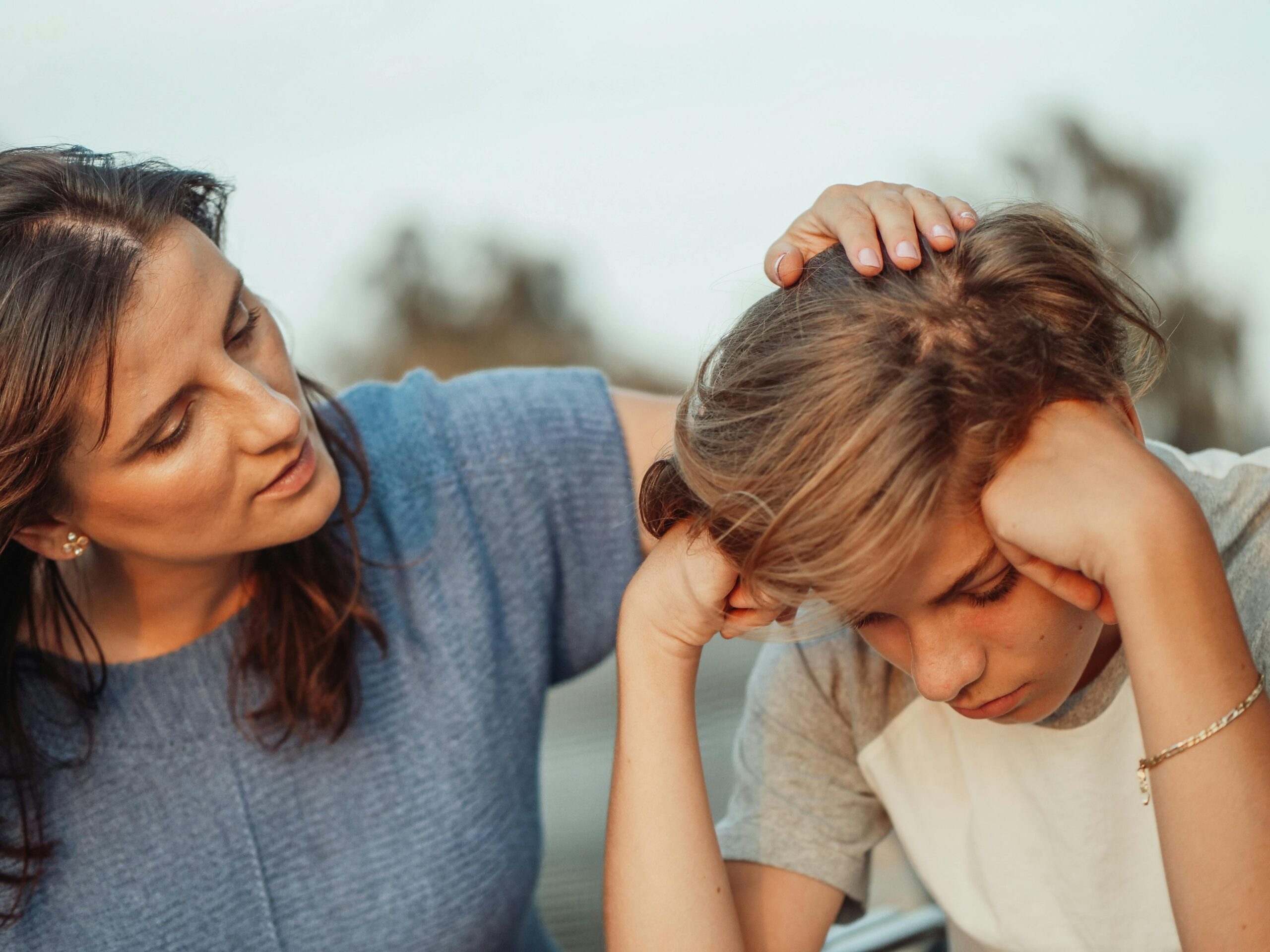 A woman comforting a distressed boy by gently touching his head.