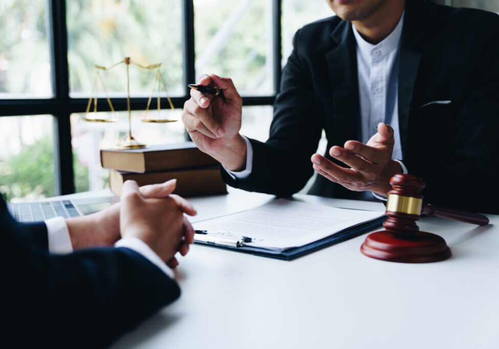 Lawyer consulting client with legal documents and gavel on table.