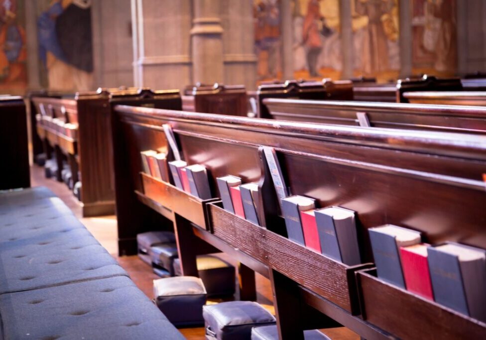 Rows of wooden church pews with hymnals and Bibles.