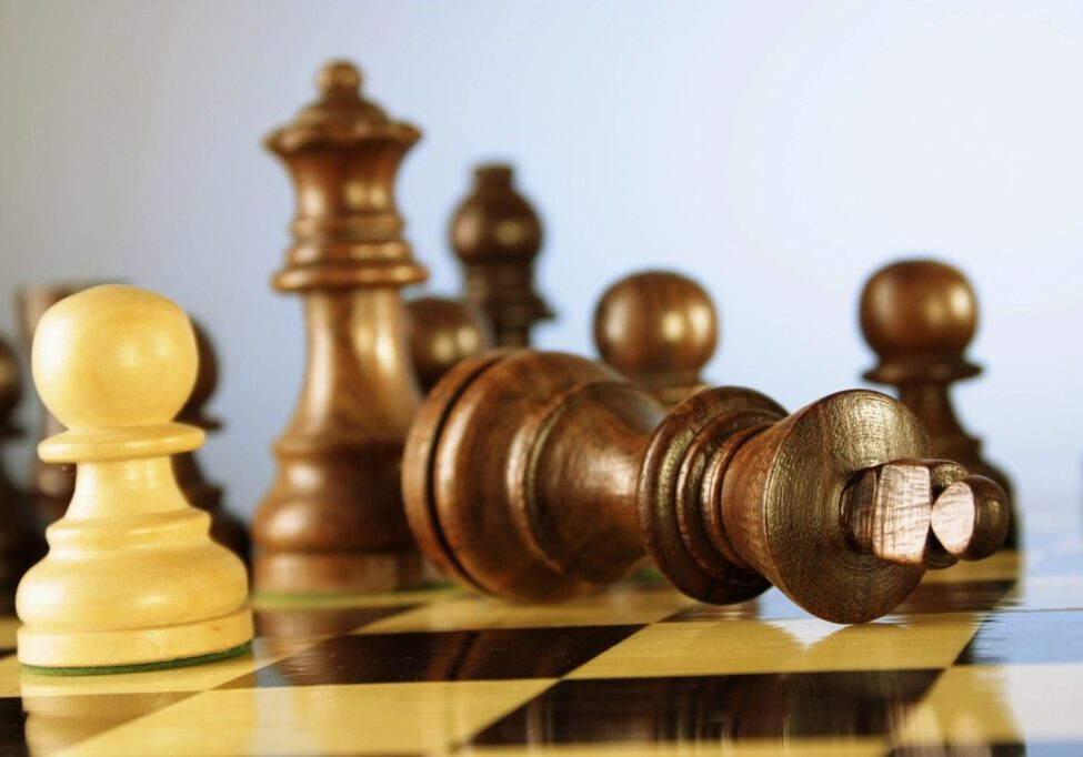 Wooden chess pieces on a board with a fallen king in focus.