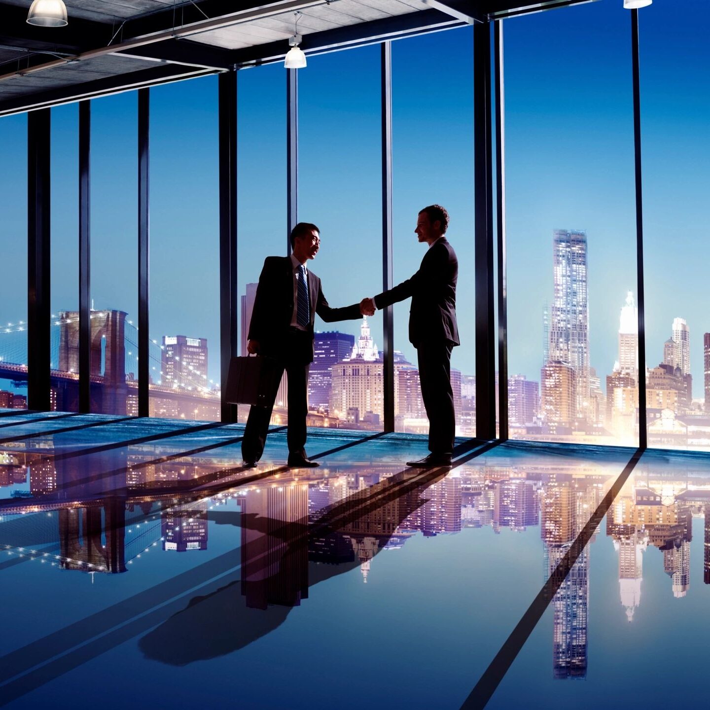 Two businessmen shaking hands in a high-rise office with a city skyline view.