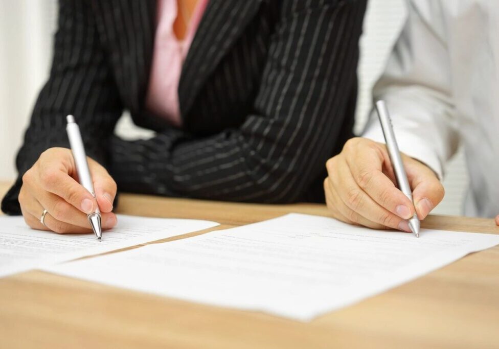Two people signing documents at a table.