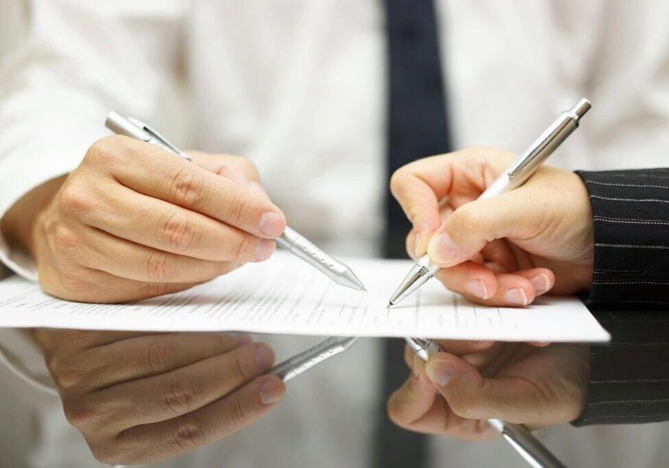 Two people signing a document with pens.