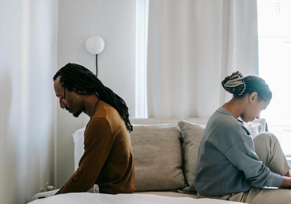Couple sitting back-to-back on a couch, appearing distant and upset.