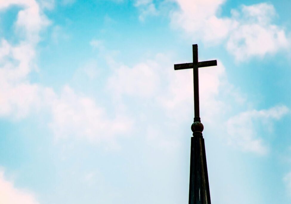 A tall church steeple with a cross against a blue sky with clouds.