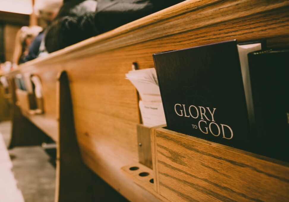 A Bible titled 'Glory to God' rests in a wooden church pew.