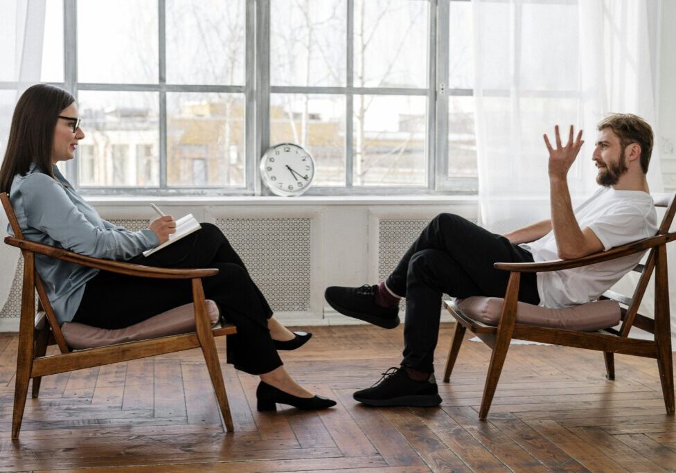 Two men in a therapy session, one gesturing while the other listens.