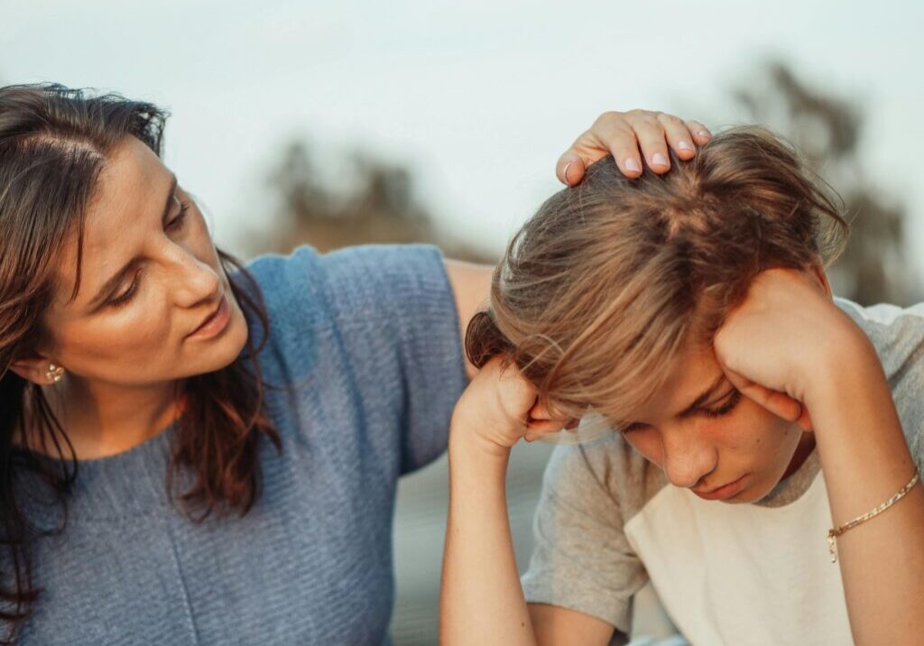 A woman comforting a distressed boy by gently touching his head.