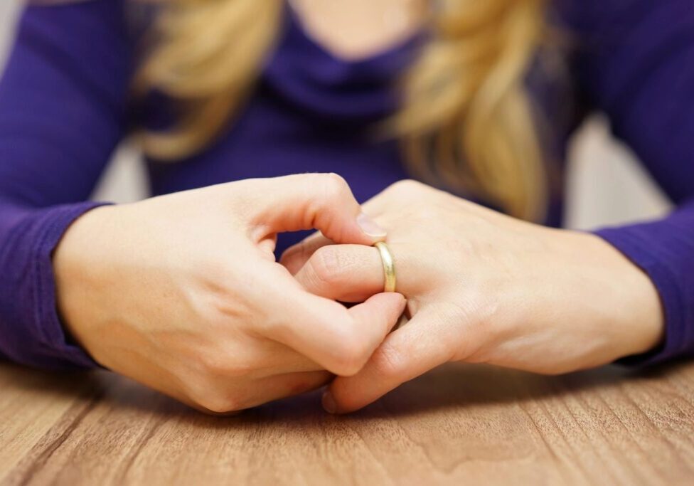 Close-up of hands with a wedding ring, fingers intertwined.